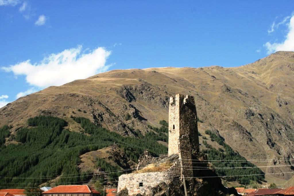 სნოს ციხის ქვის კოშკი კლდეზე, სოფლის სახლებისა და მთების ფონზე